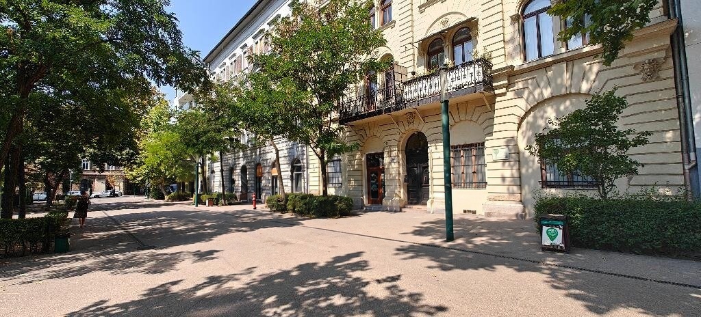 Elegáns, klasszikus homlokzat kovácsoltvas erkélykorláttal egy fás utcában